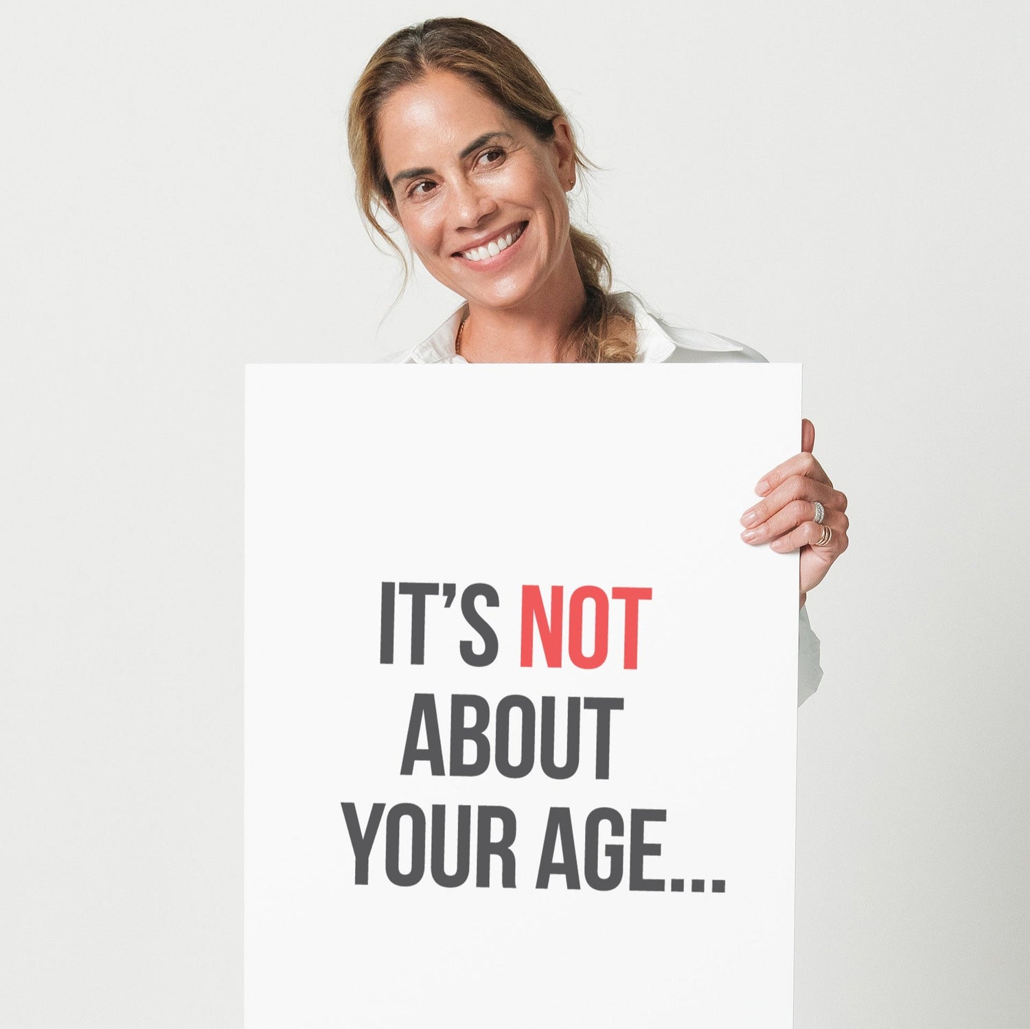 A woman in a white shirt holding a sign that says "It's not about your age."