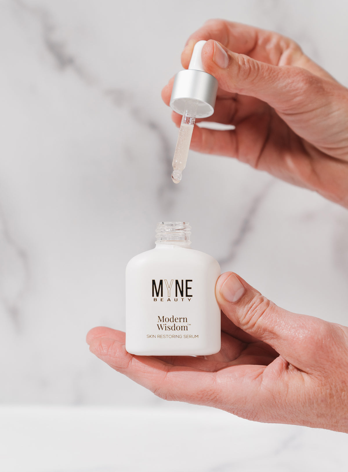 A person holding a small bottle of Modern Wisdom skin restoring serum in one hand and the bottle's eyedropper top in the other., t4