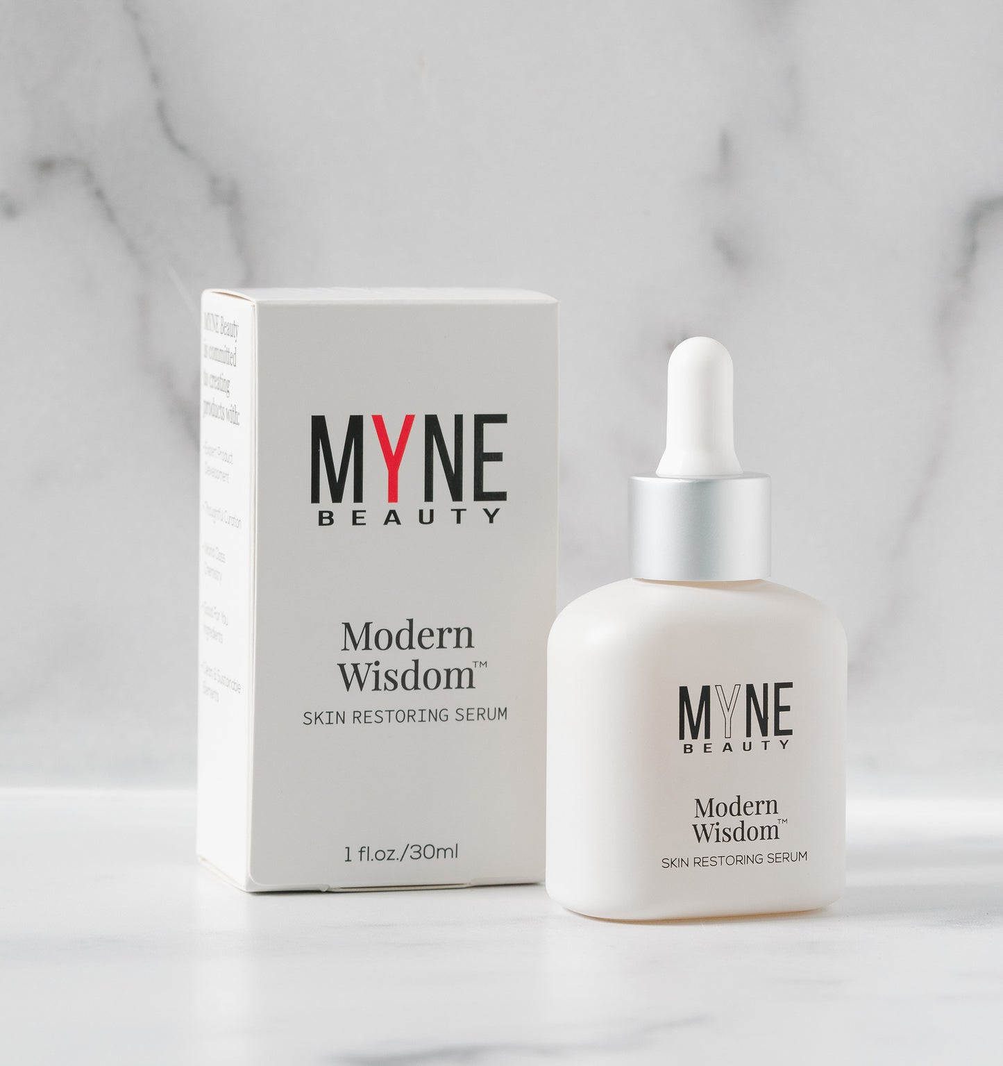 A small bottle of Modern Wisdom skin restoring serum propped up next to its packaging box. Both the box and bottle have the Myne Beauty logo on them.