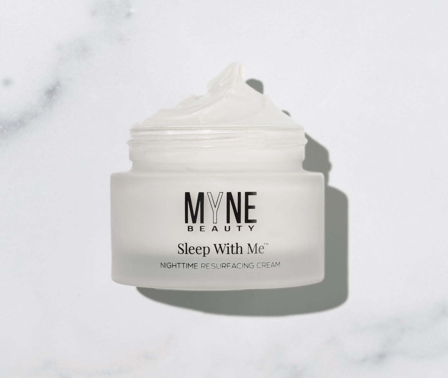 A jar of Sleep With Me Nighttime Resurfacing Cream from Myne Beauty laid on its side against a white marble countertop.