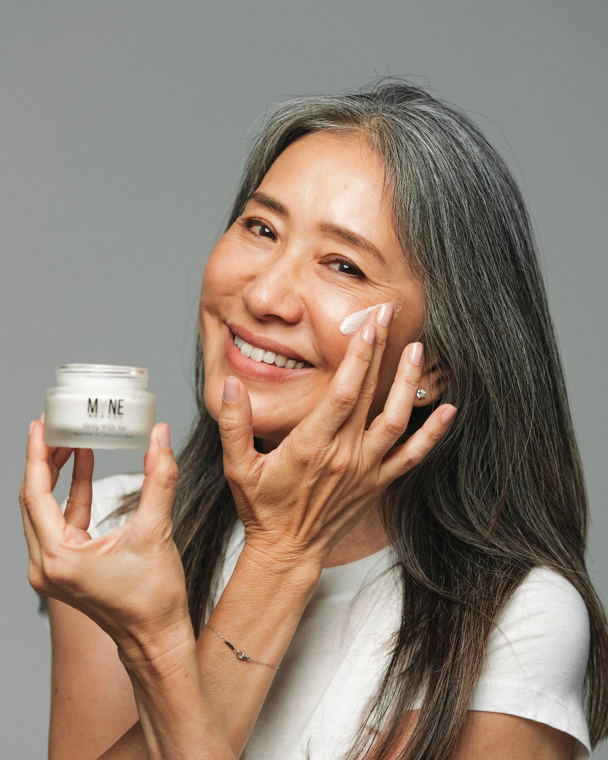 Woman smoothing Sleep With Me night cream onto her cheek, t4